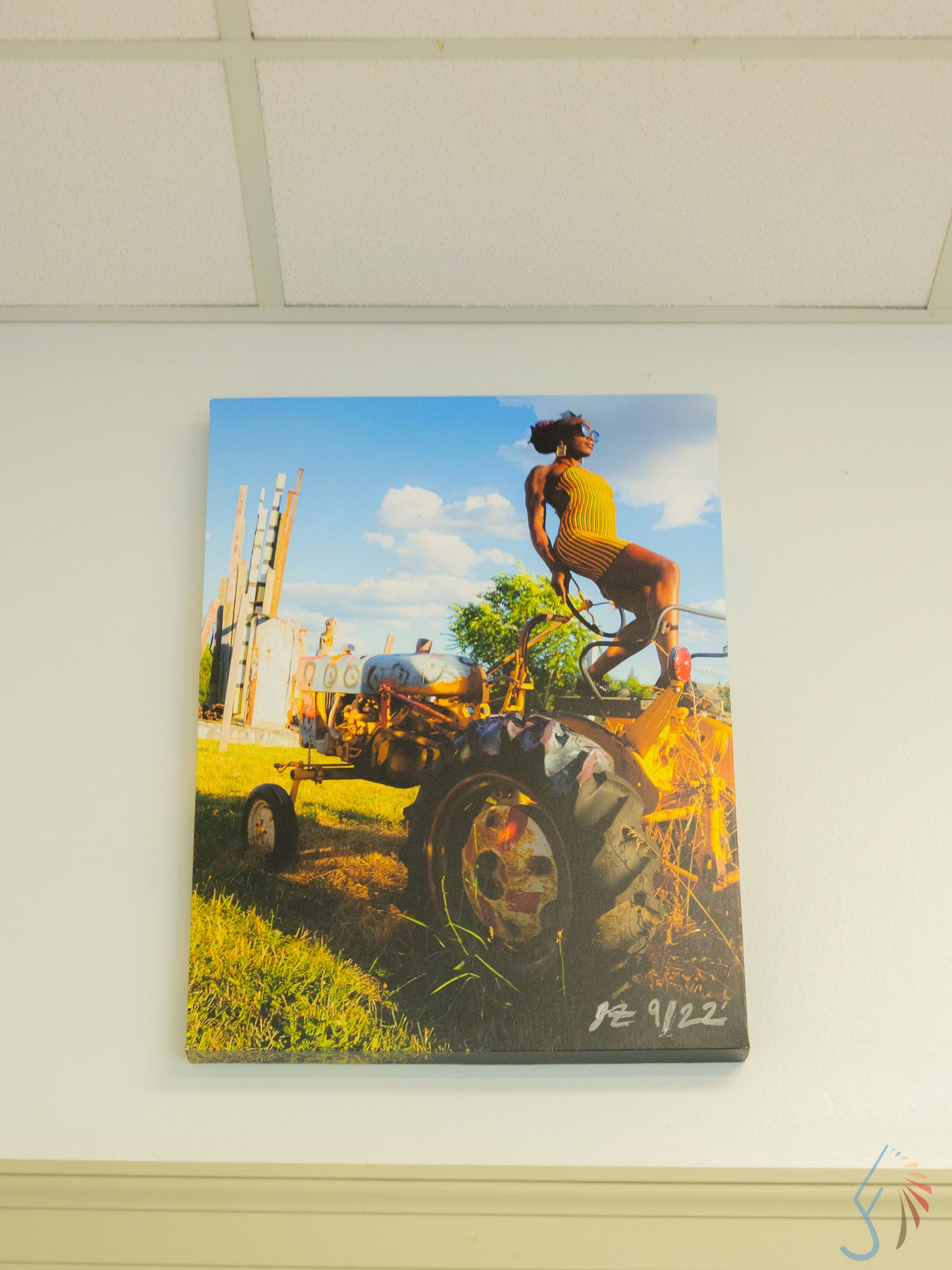 Canvas print of a woman posing on a vintage tractor in a vibrant outdoor scene with blue skies and greenery.