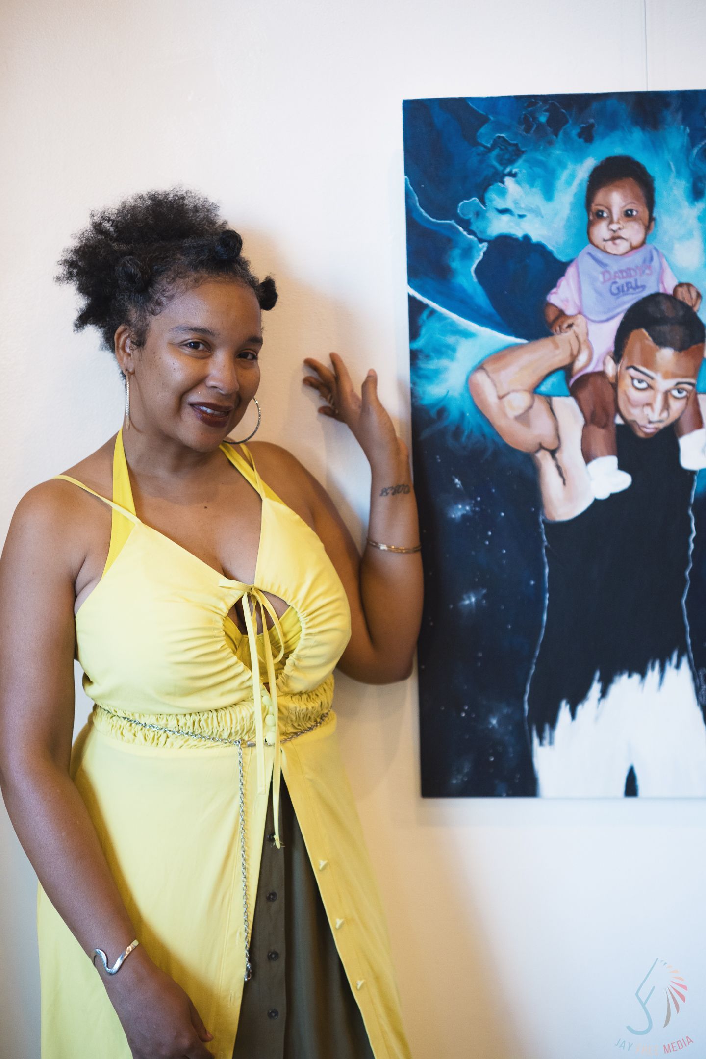 Woman in yellow halter dress poses beside colorful portrait painting at art gallery.
