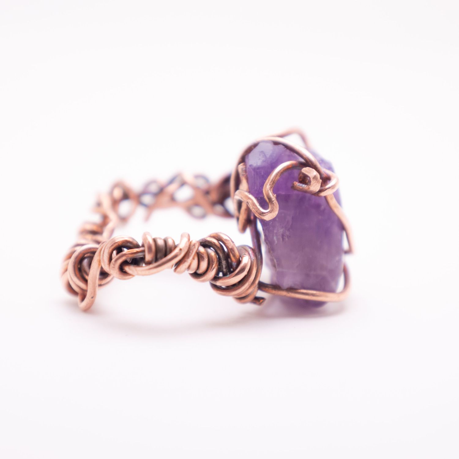 Handmade copper wire wrapped ring with a raw purple amethyst crystal stone and intricate woven band.