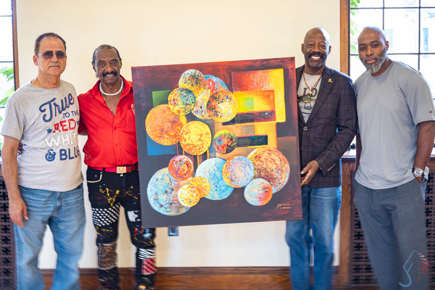 Four men proudly display a vibrant colorful abstract painting featuring spheres at an indoor art exhibition.
