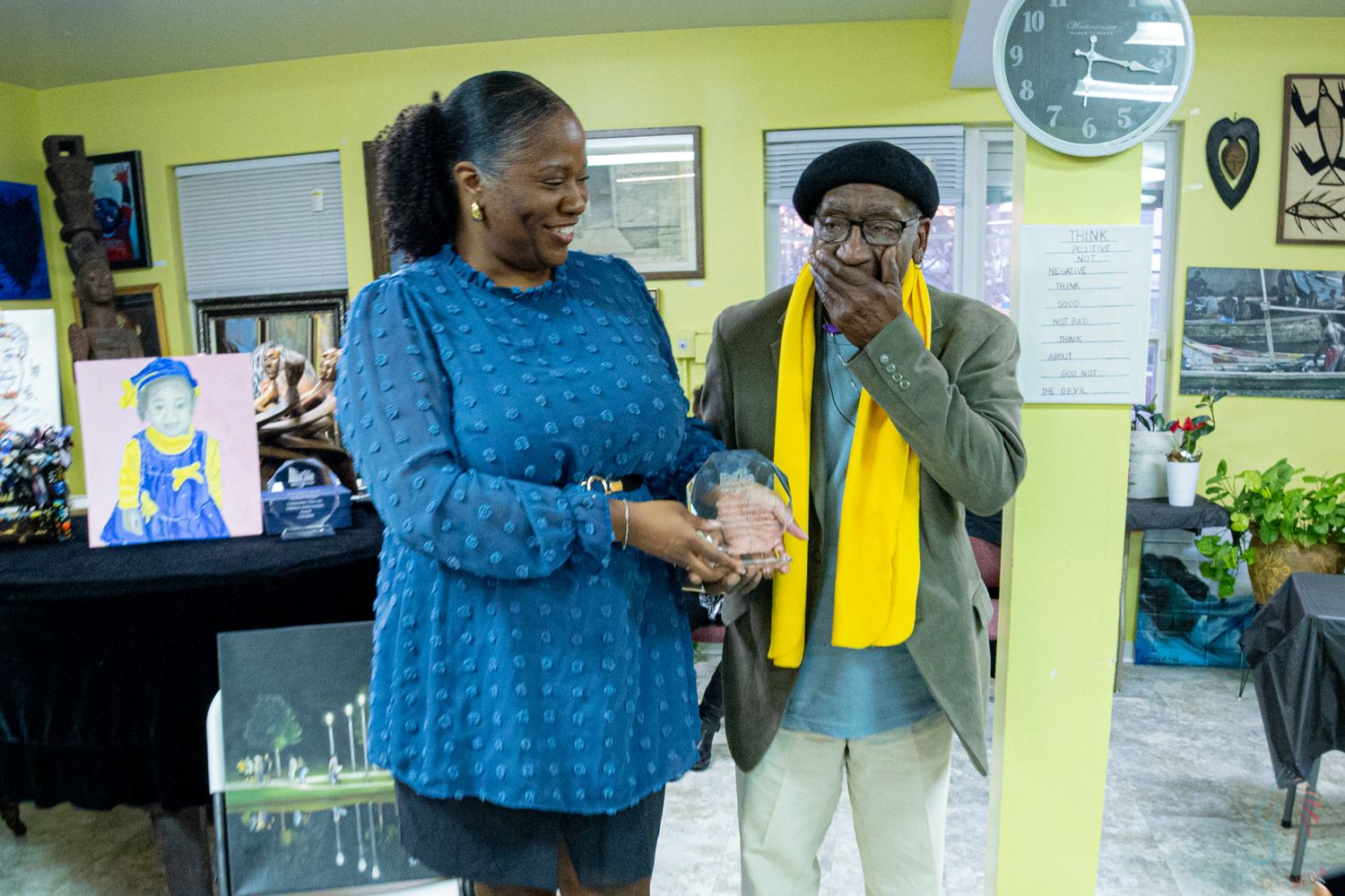 Two people sharing a joyful moment indoors, one holding an award, with a portrait and candles visible in the background.