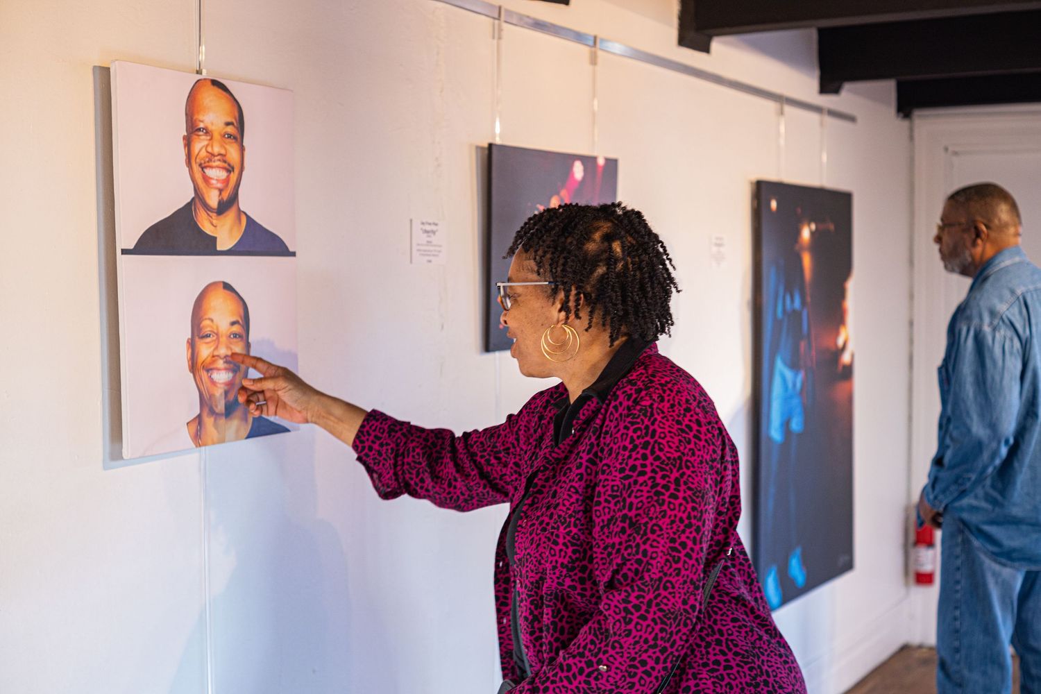 Woman pointing at portrait photograph on gallery wall during an indoor art exhibition.