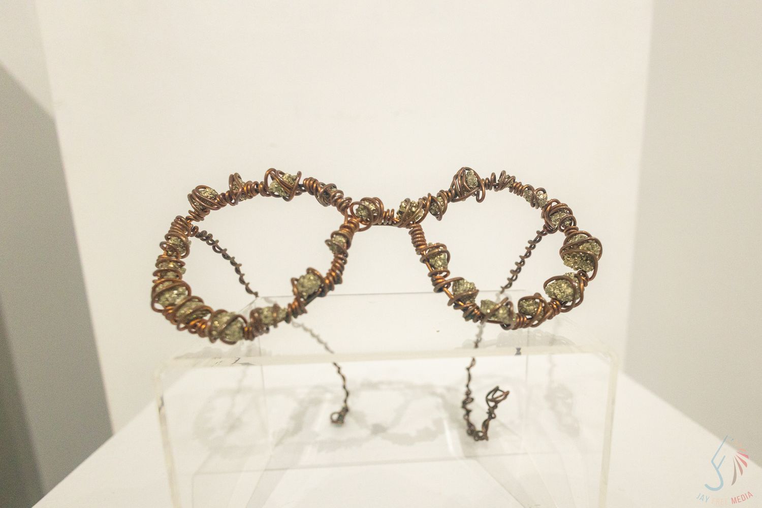 Artistic eyeglasses sculpture made from twisted wire and small stones displayed on a clear acrylic stand.
