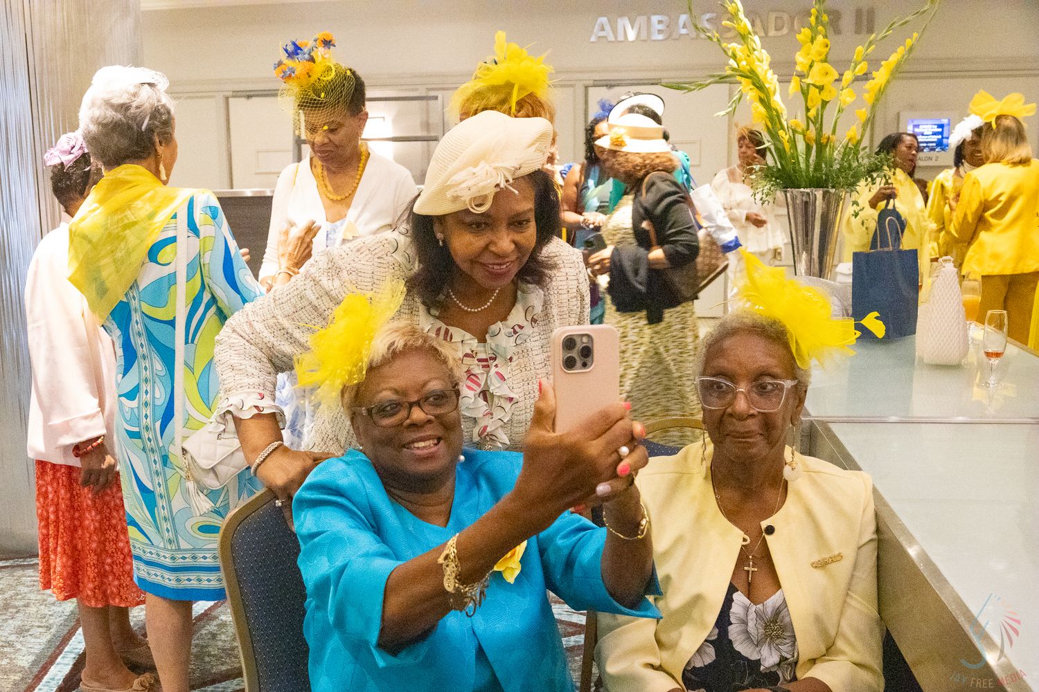 Elderly women wearing yellow feathered hats take a selfie at a festive gathering.