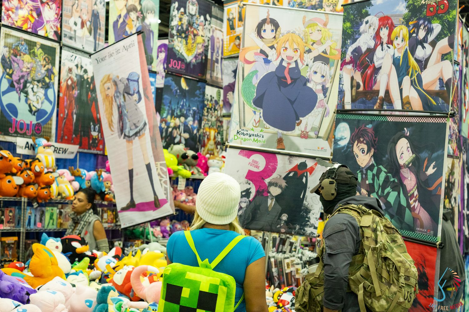 Anime convention vendor booth displaying colorful manga posters, plush toys, and merchandise.