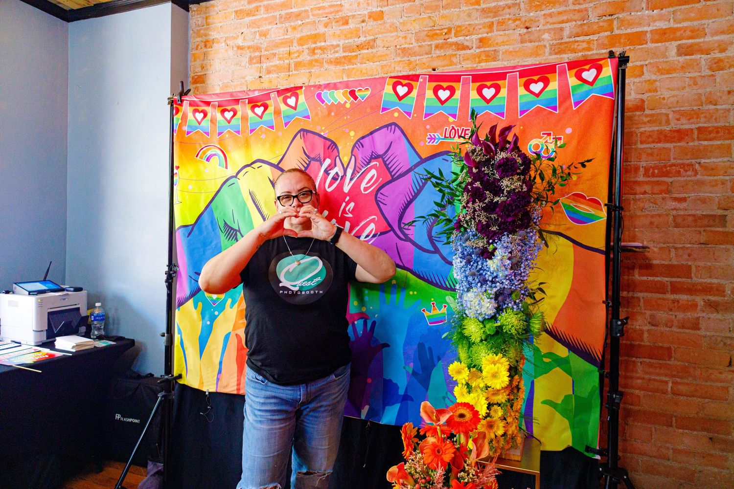Person posing in front of colorful love-themed mural with floral arrangement in vibrant art studio.