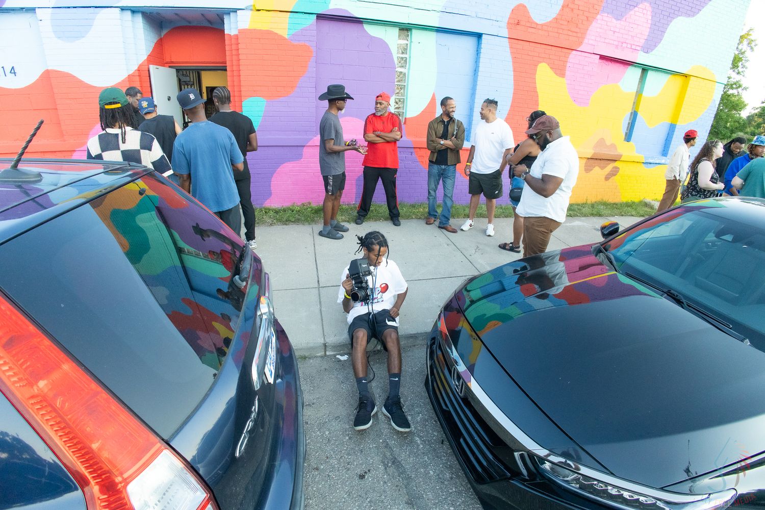 Group of people gathered outside a building with a colorful mural at an outdoor event.