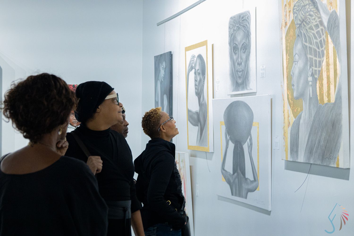 Three people in black clothing view contemporary portrait artwork displayed on a white gallery wall.
