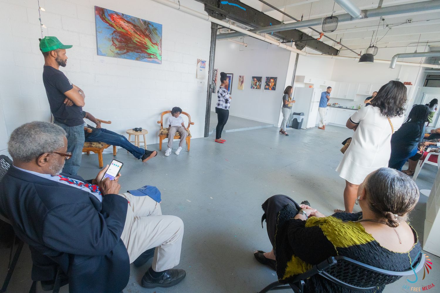 People gathered in a bright art gallery space, viewing colorful paintings on white walls during a casual exhibition event.
