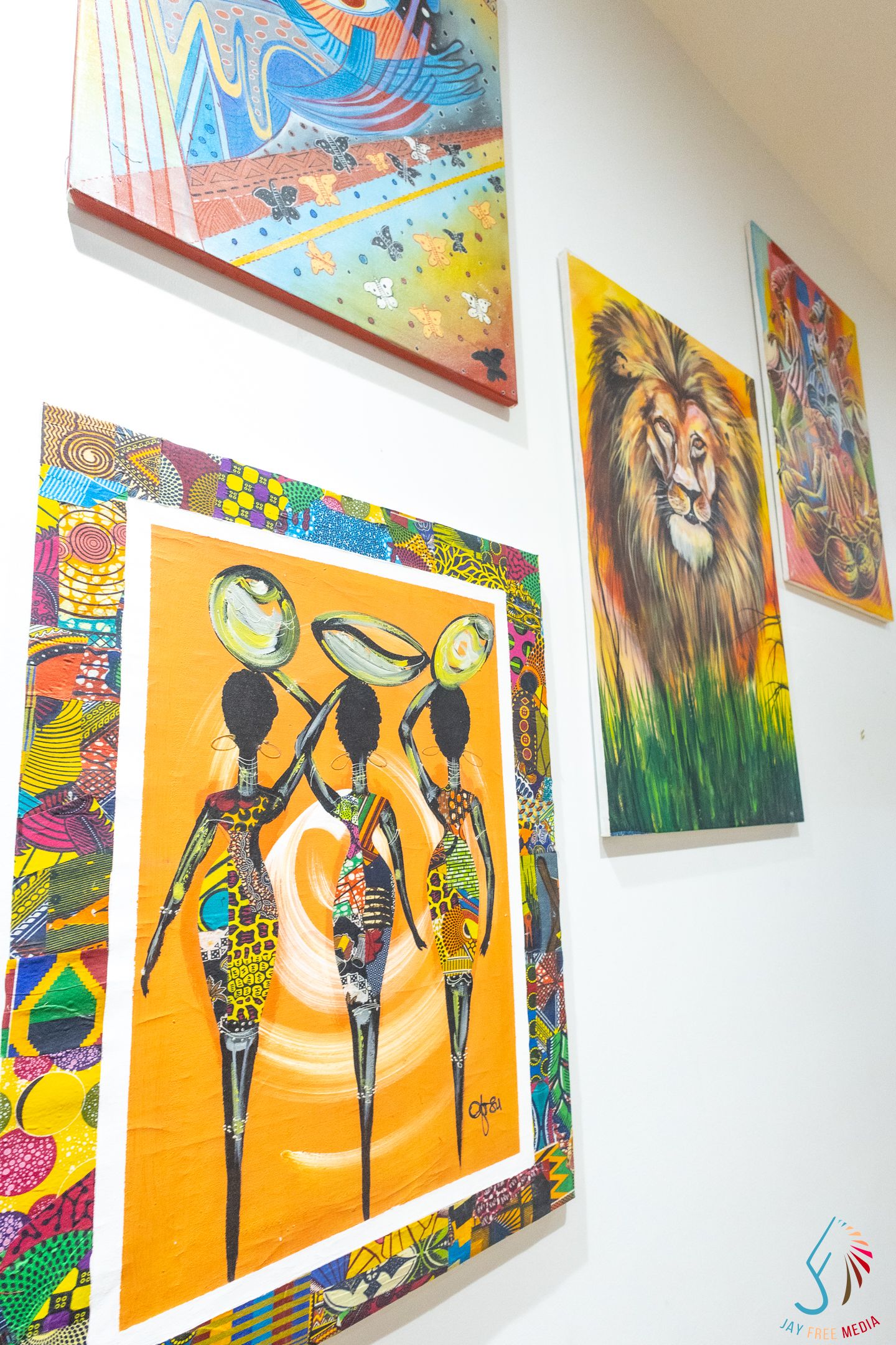 Colorful art gallery wall displaying African-inspired paintings including women carrying bowls and a vibrant lion portrait.
