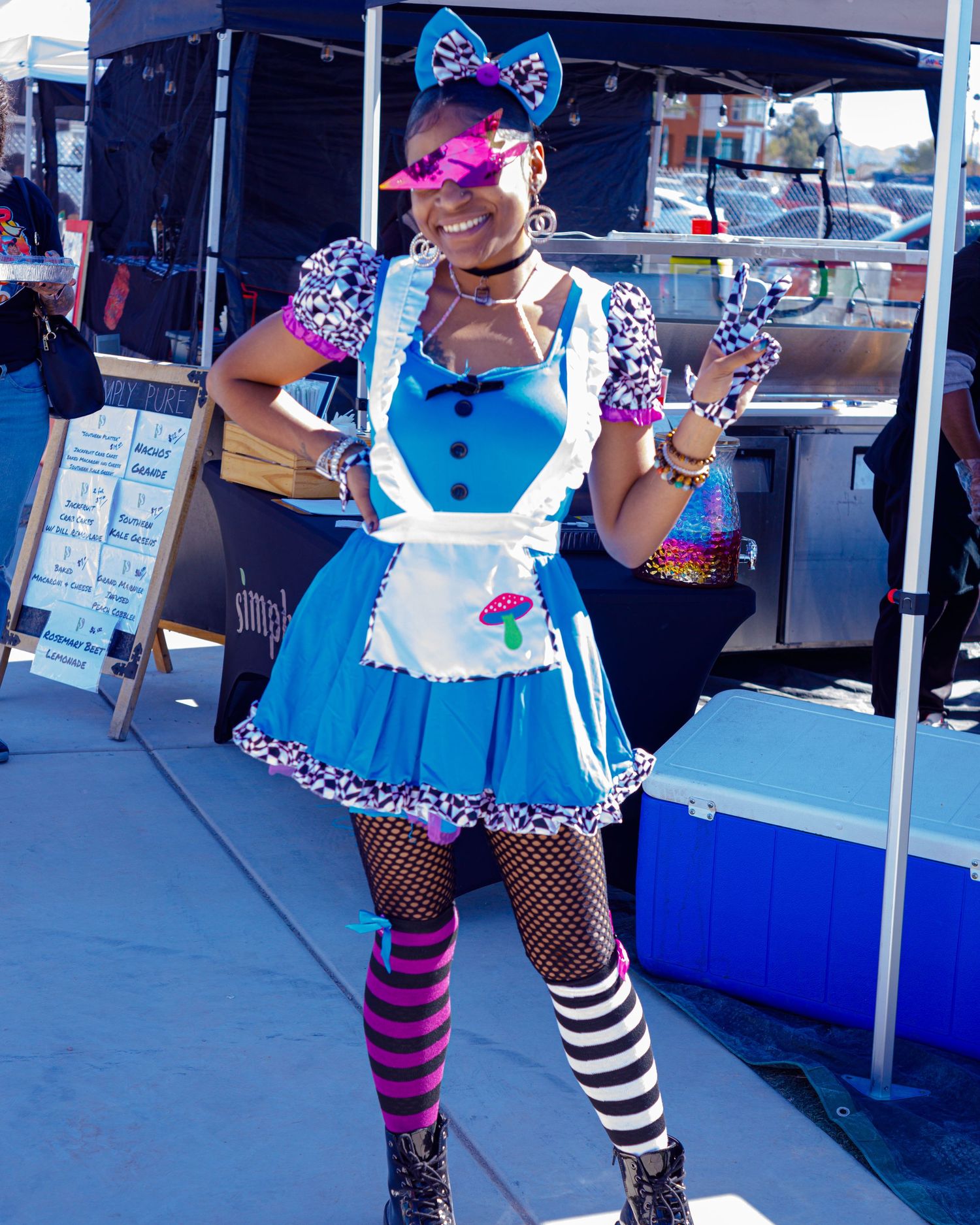 Woman in Alice in Wonderland costume with blue dress, fishnet stockings, and striped socks at outdoor festival.