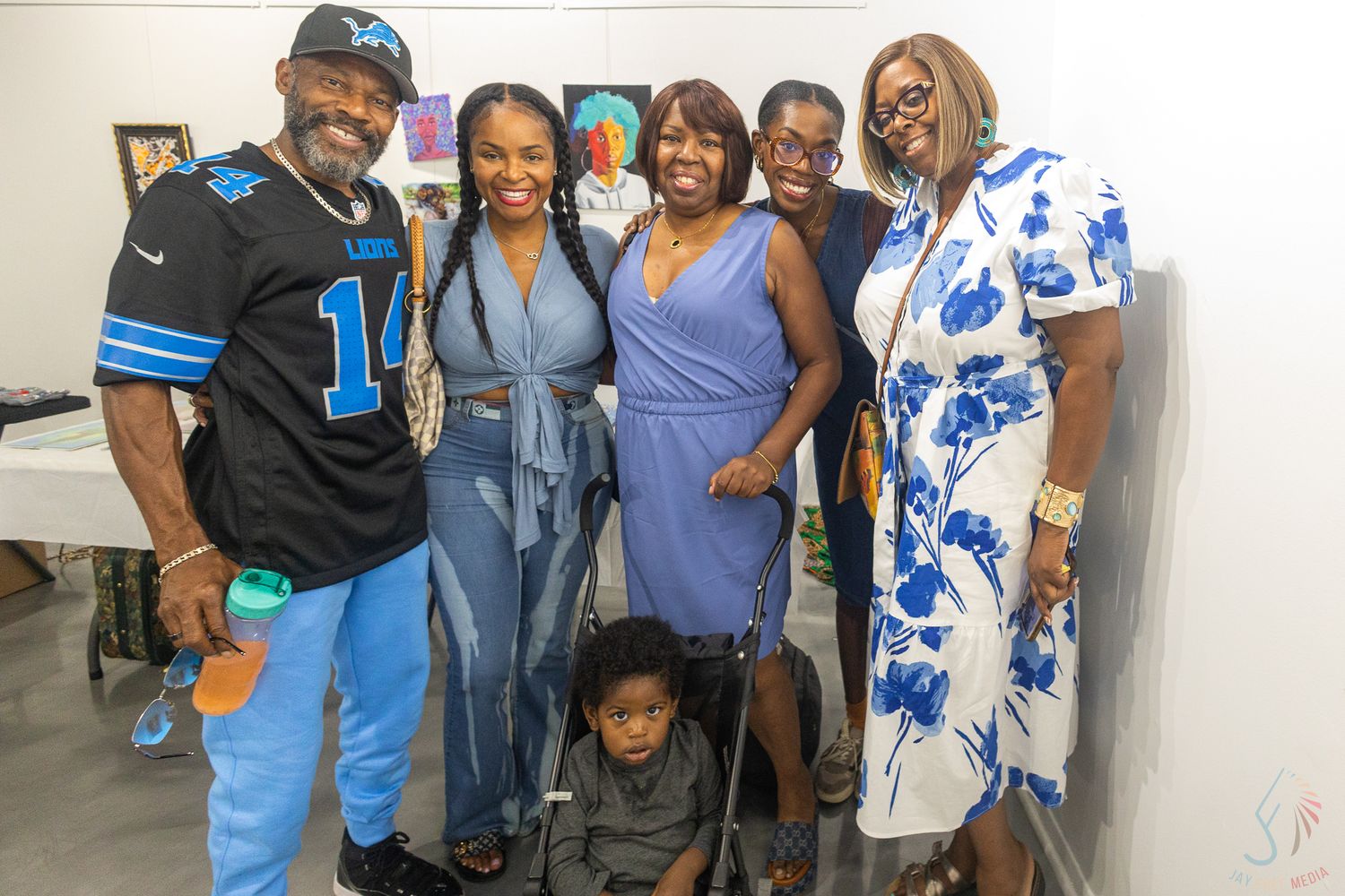 A joyful group of six Black adults and a child posing together at an indoor art gallery event.