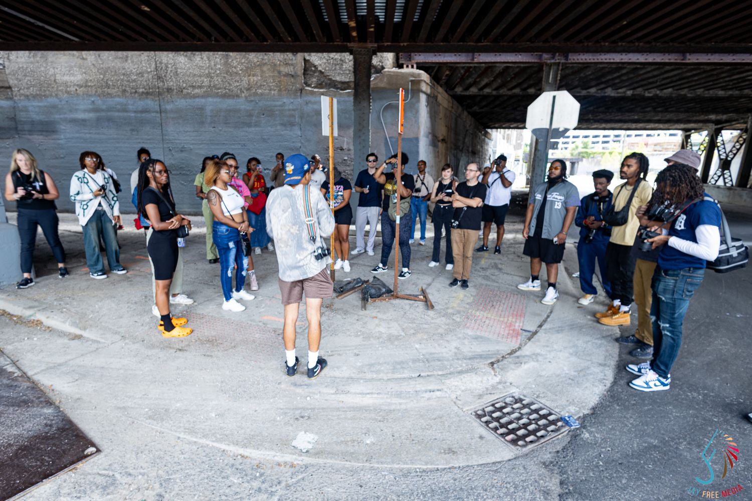 Group of young people gathered in a circle under a bridge overpass during an outdoor urban event.