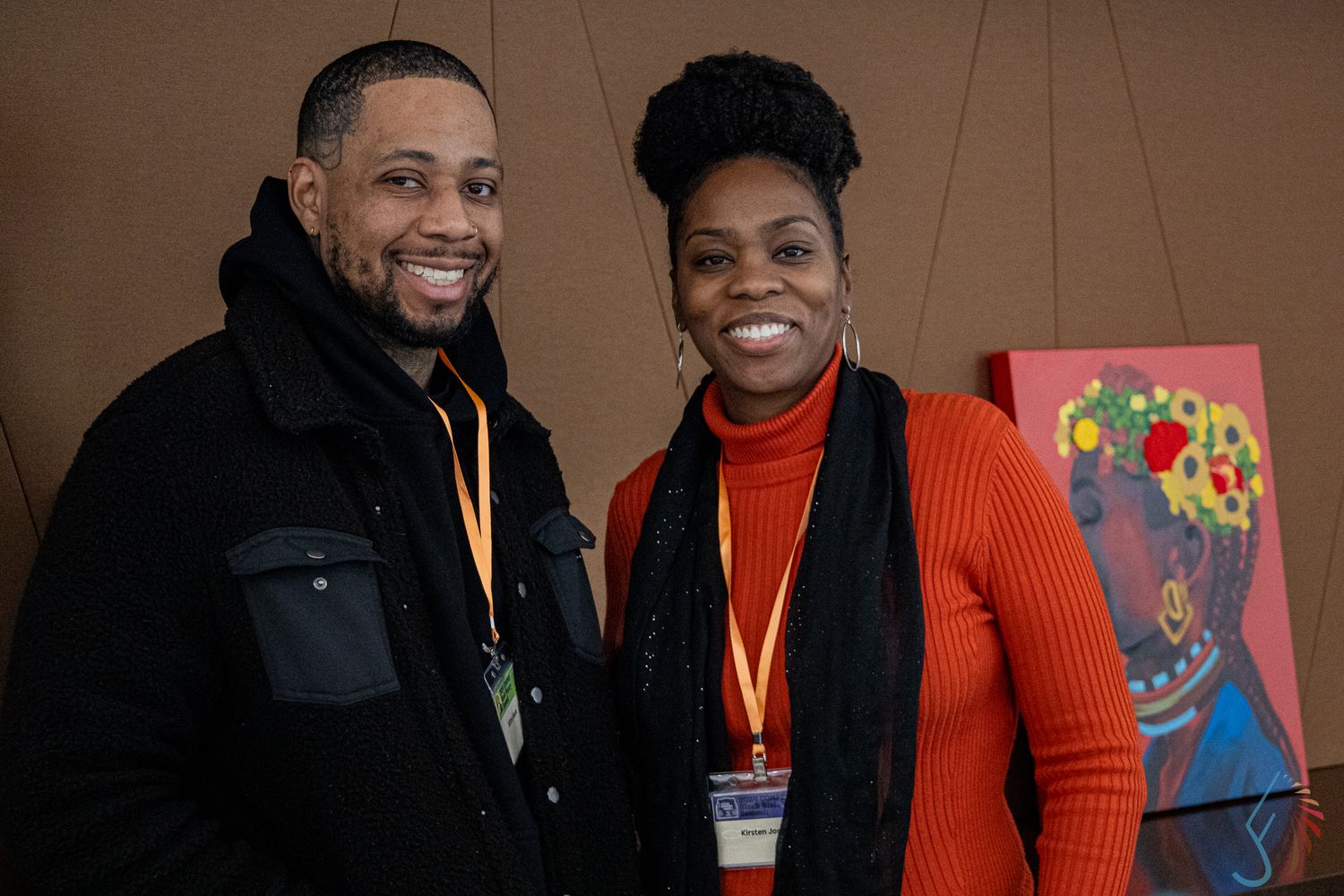 Two smiling professionals wearing lanyards pose together at an indoor event with colorful artwork in the background.
