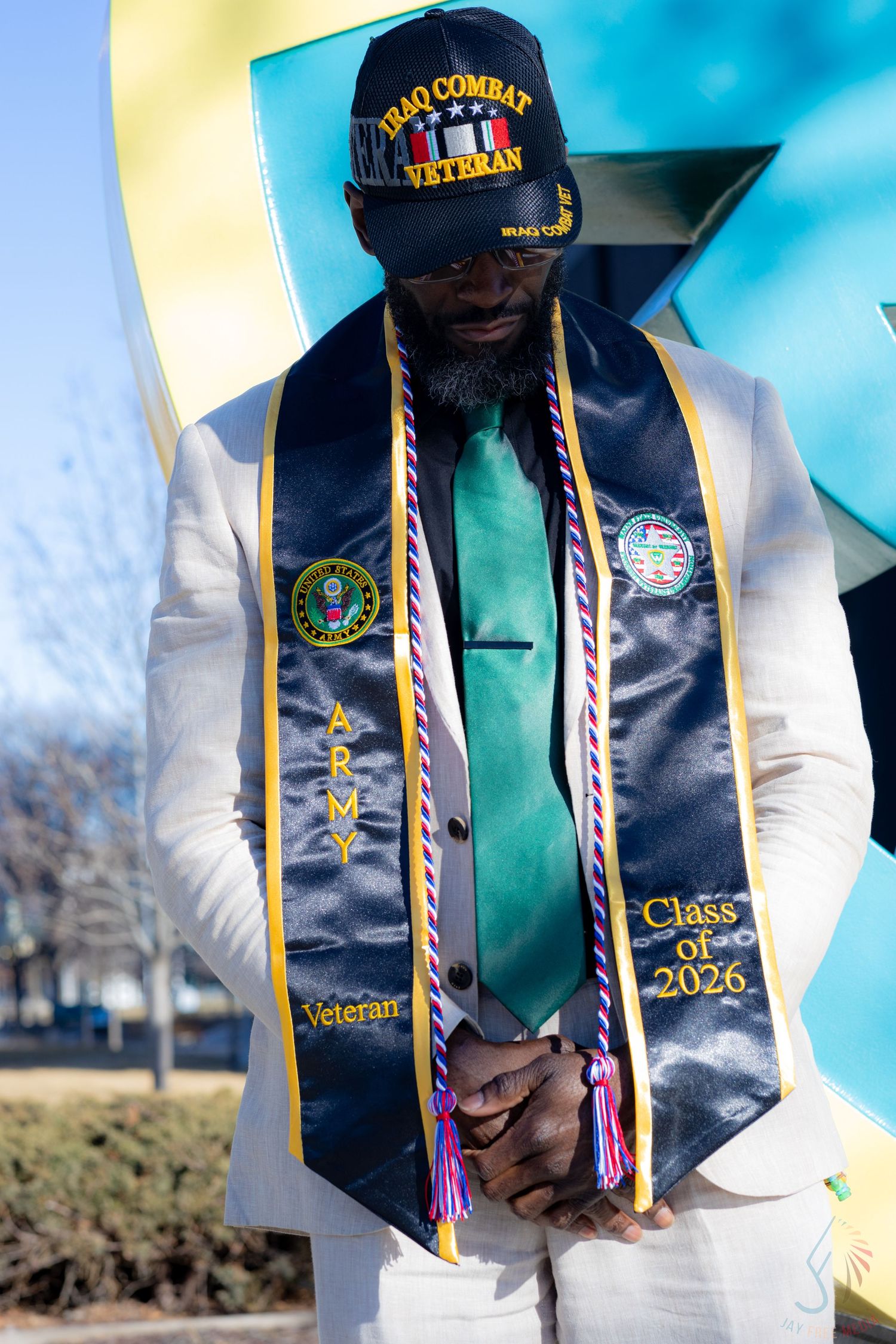 Iraq Combat Veteran wearing Army graduation stole reading Class of 2026, dressed in white suit with green tie.