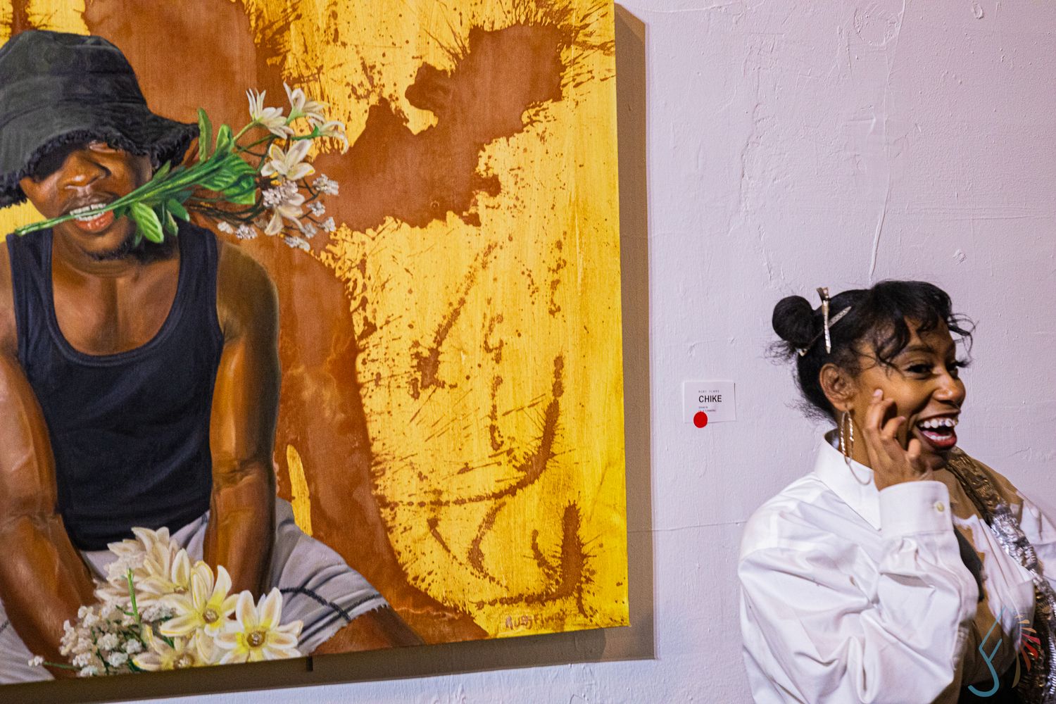 Woman laughing beside a vibrant painting of a person holding white flowers at an art gallery.