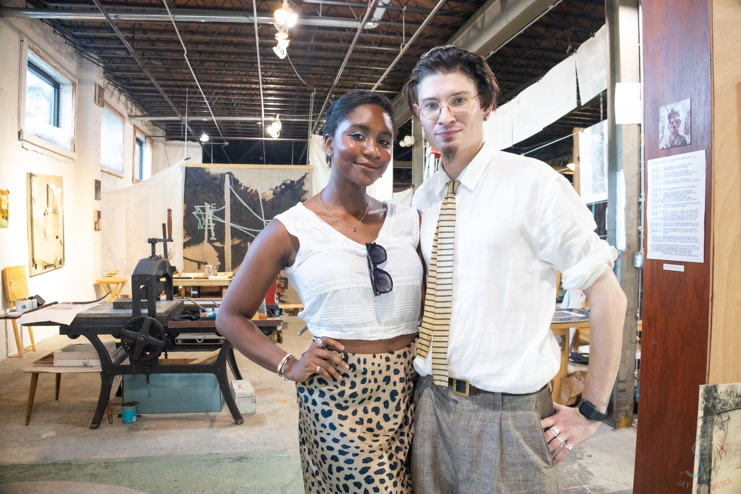 A woman in a leopard skirt and a man in a tie pose together smiling inside an art studio workshop.