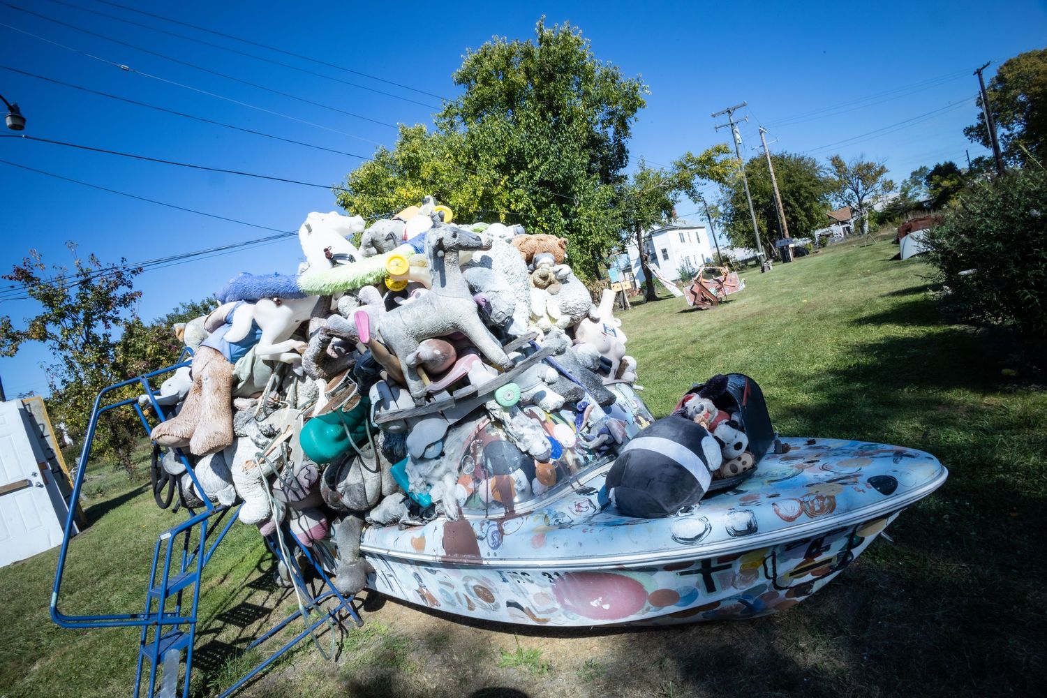 Colorful junk art sculpture overflowing with toys and debris in a boat displayed outdoors under a clear blue sky.