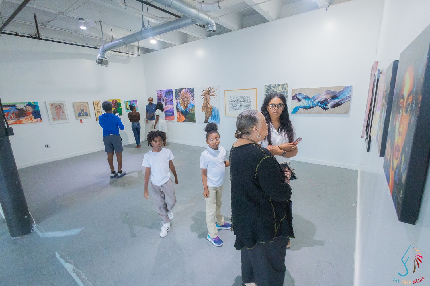 Visitors explore colorful artwork displayed on white gallery walls during an art exhibition opening event.