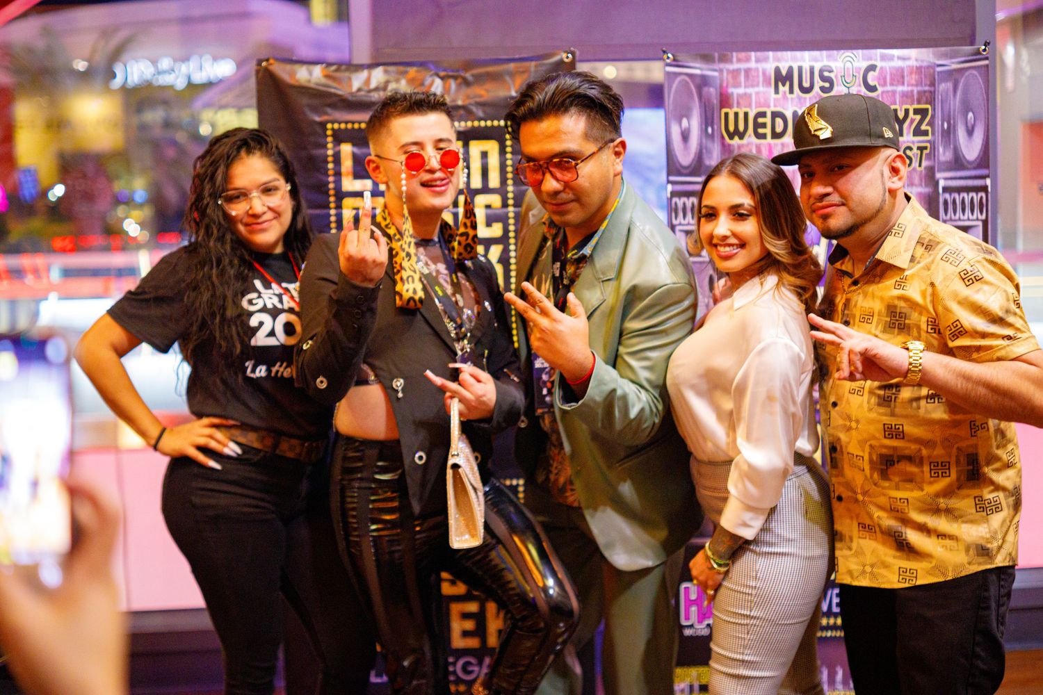 Group of five people posing and smiling together at a lively Latin music event indoors.