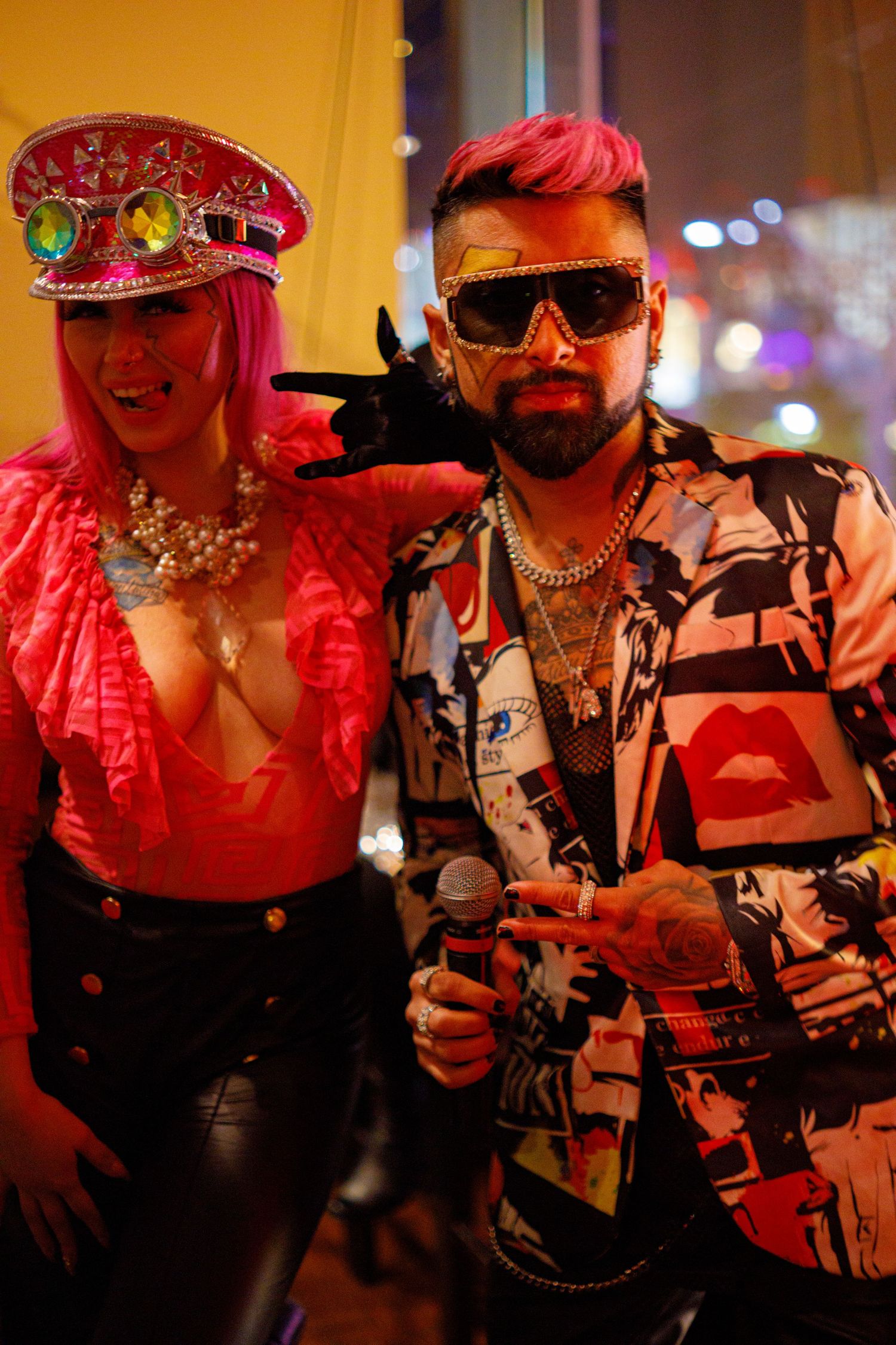 Two colorfully dressed performers pose at a vibrant nightclub event, wearing bold accessories and stylish outfits.