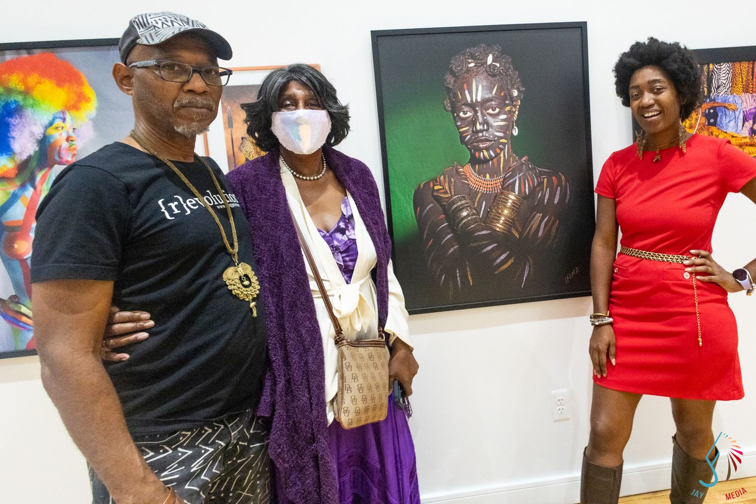 Three people posing at an art gallery exhibition featuring vibrant African-inspired portrait artwork on white walls.