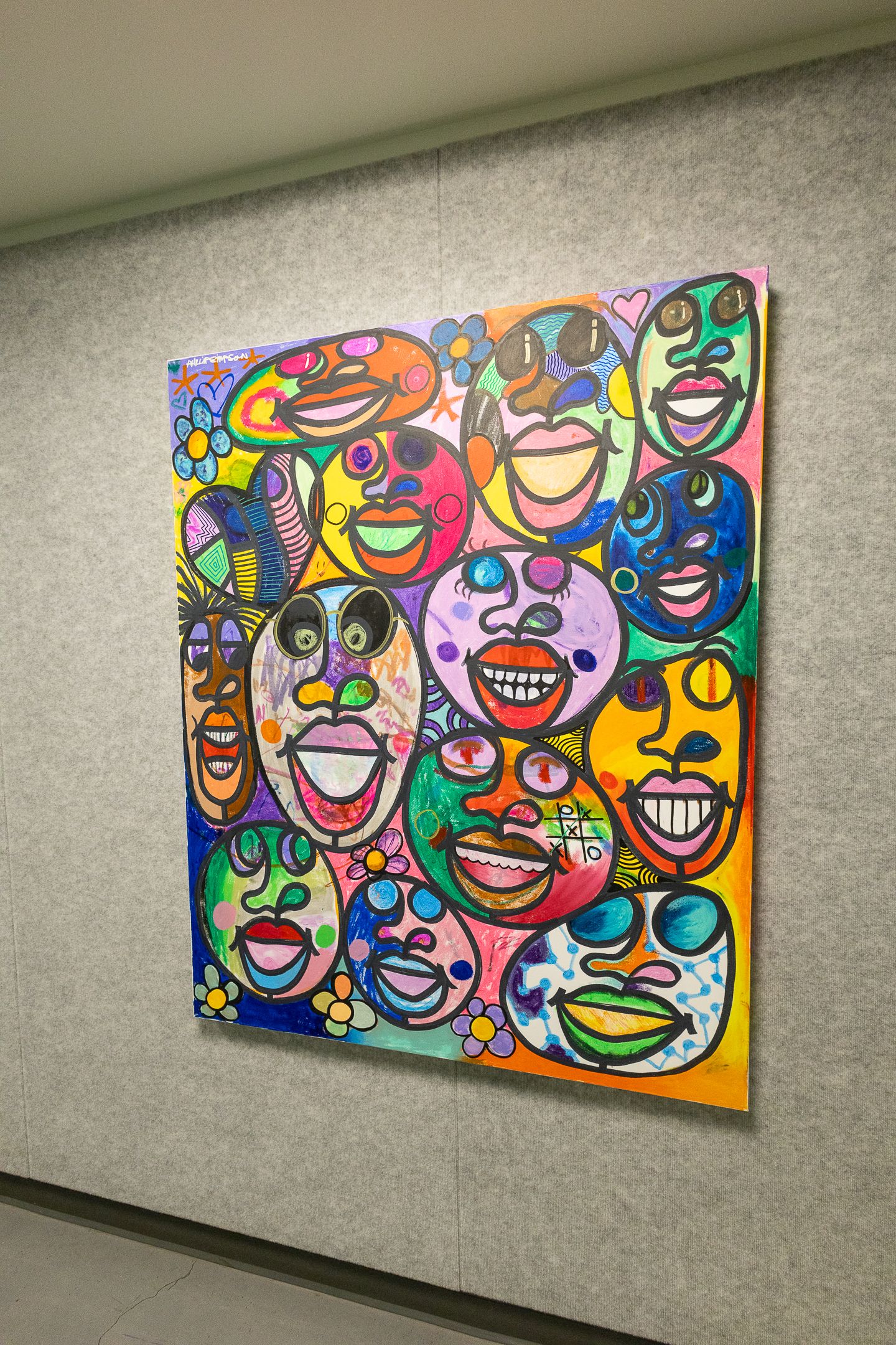 Colorful pop art painting featuring expressive cartoon faces with bold colors displayed on a gallery wall.