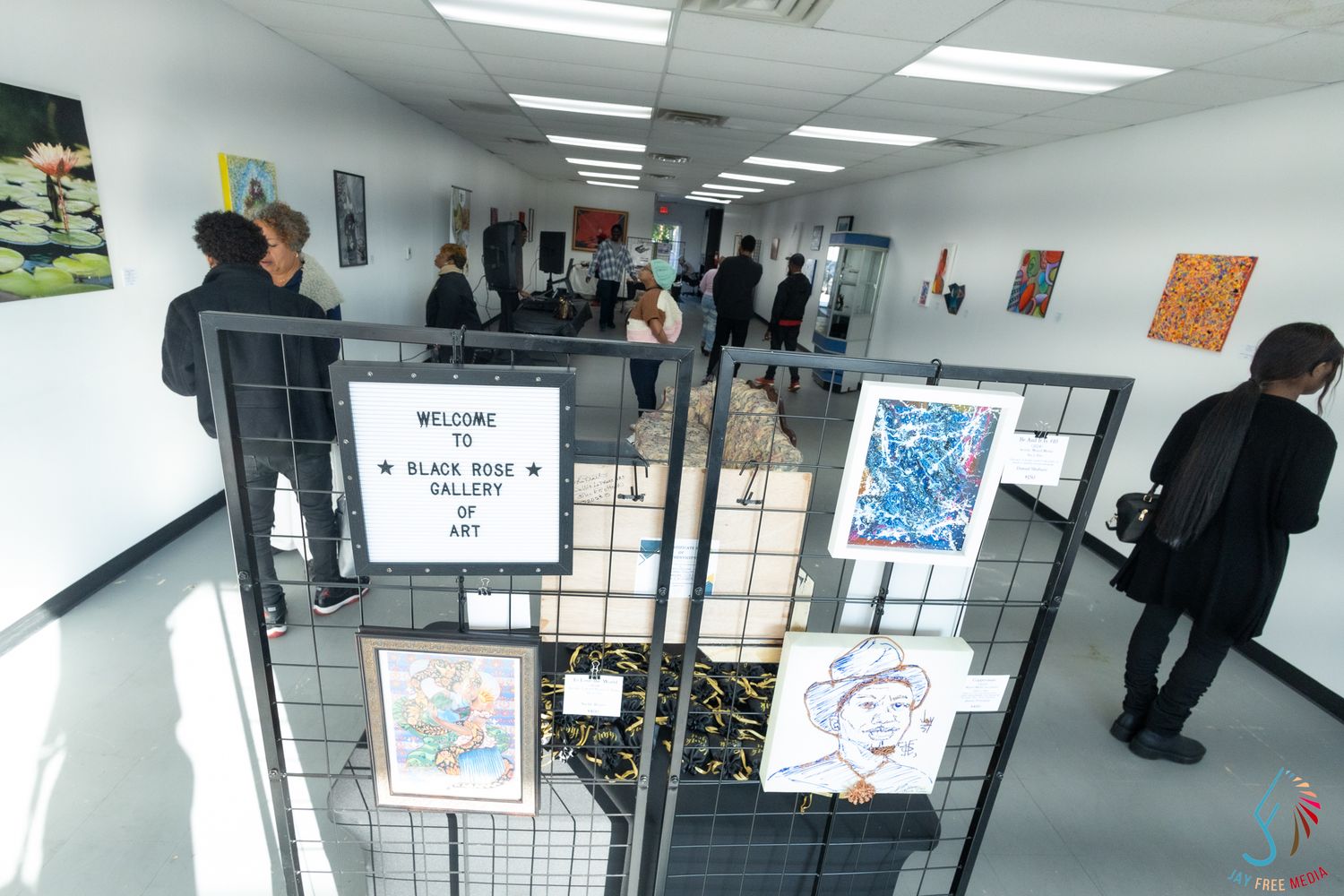 Interior view of Black Rose Gallery of Art with visitors browsing colorful artwork displayed on white walls.