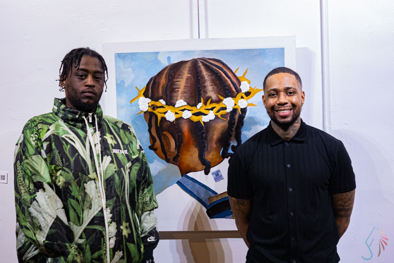 Two men pose in front of portrait painting with floral crown at art exhibition.