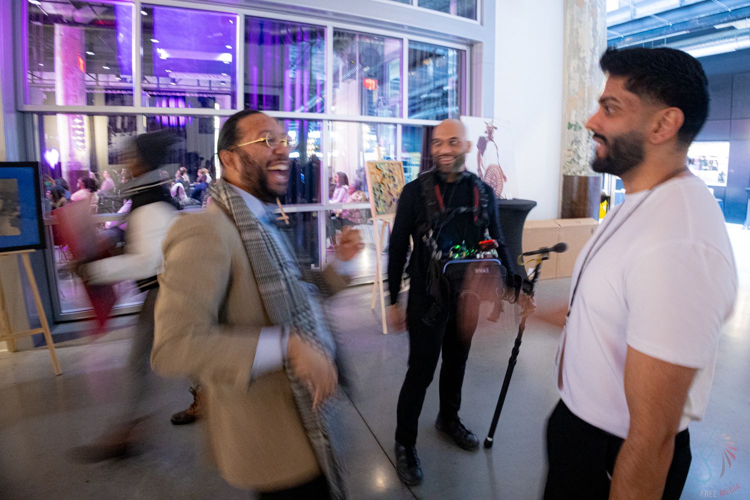 Group of four men laughing and socializing in a vibrant event venue with purple ambient lighting.