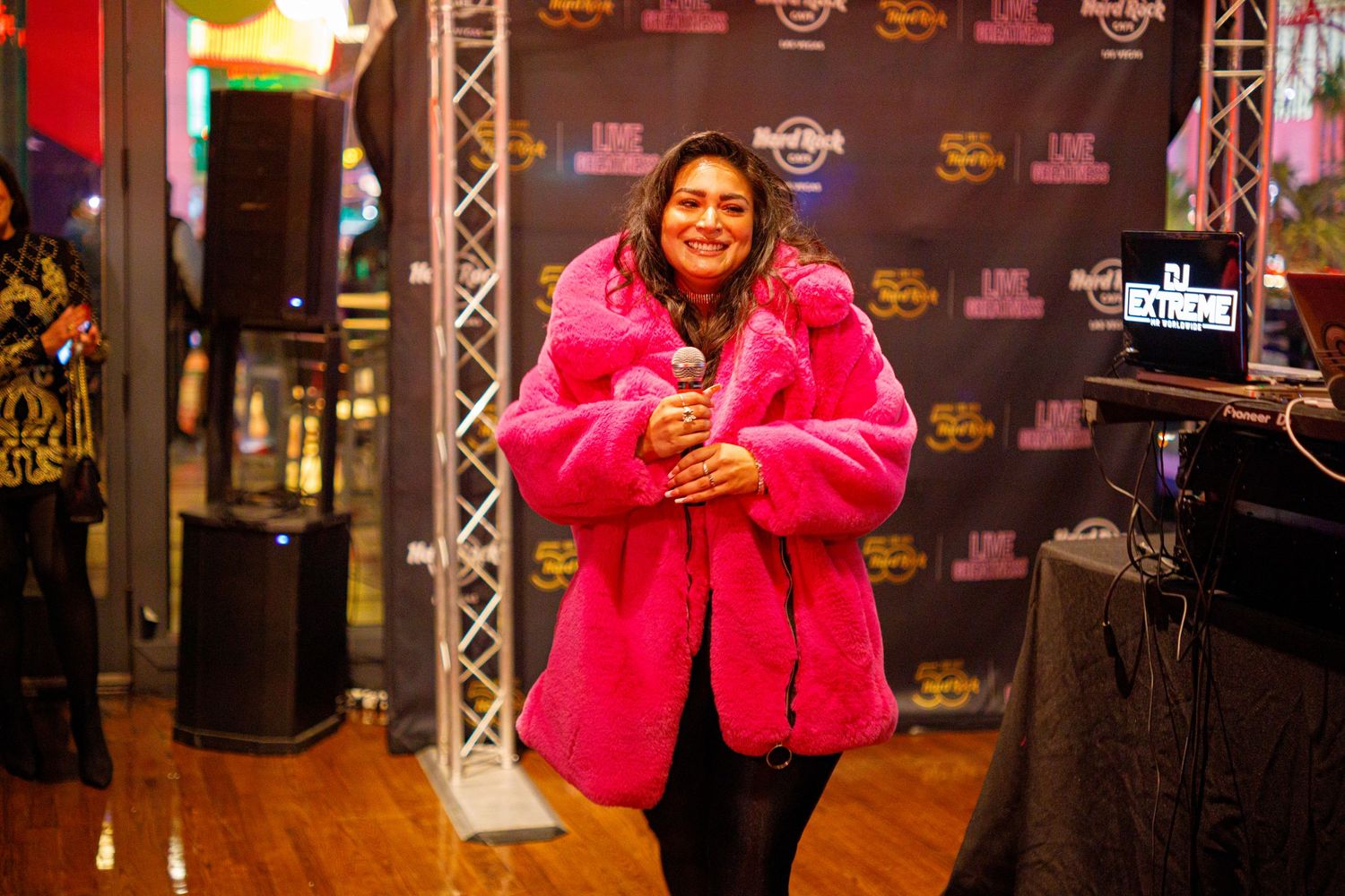 Woman in bright pink faux fur coat smiling at Latin Music Week event at Hard Rock venue.