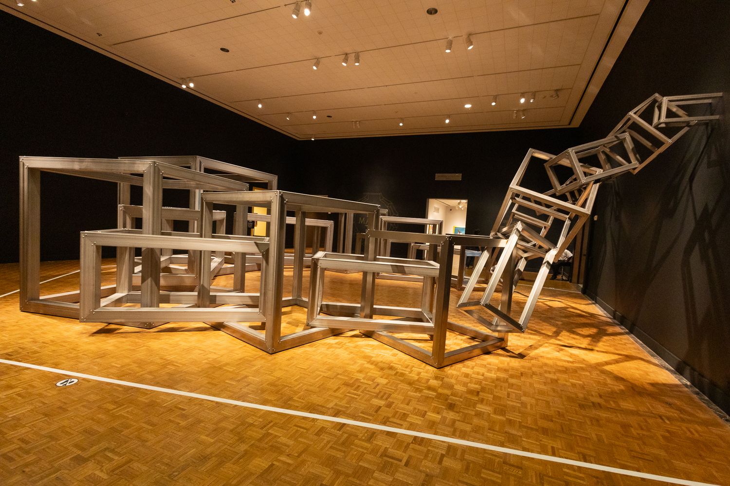 Large metal cube sculptures arranged on a parquet floor in a dimly lit museum gallery.