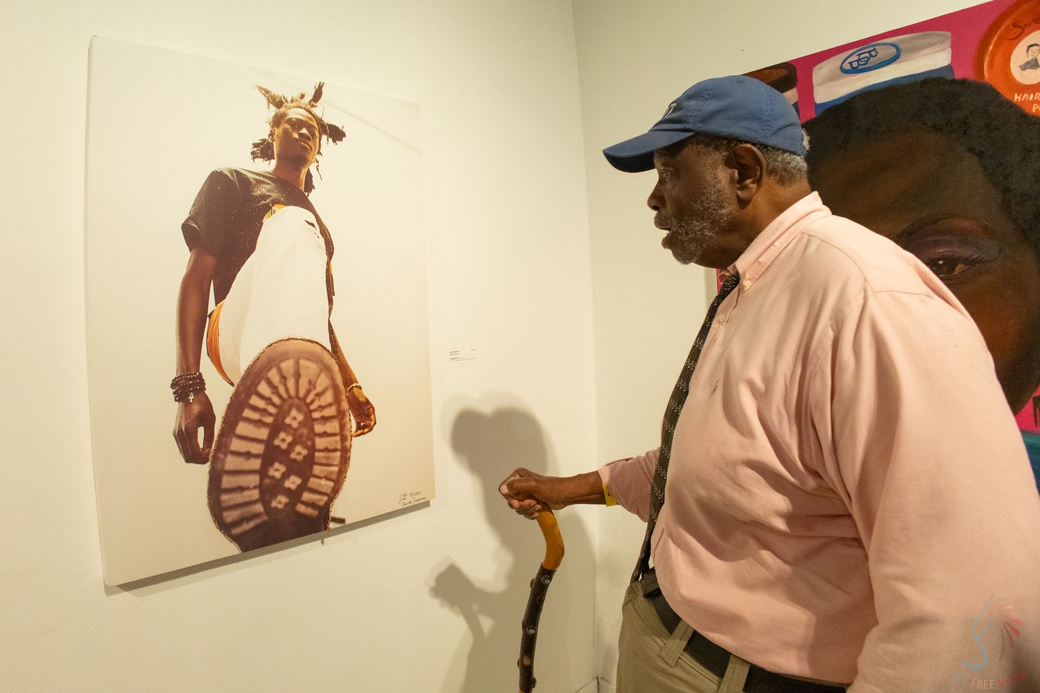 Elderly man with cane examines colorful painting of cow at art gallery exhibition.