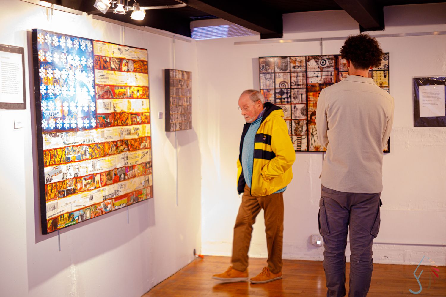 Two visitors examining colorful mosaic artwork displayed on white gallery walls during an art exhibition.
