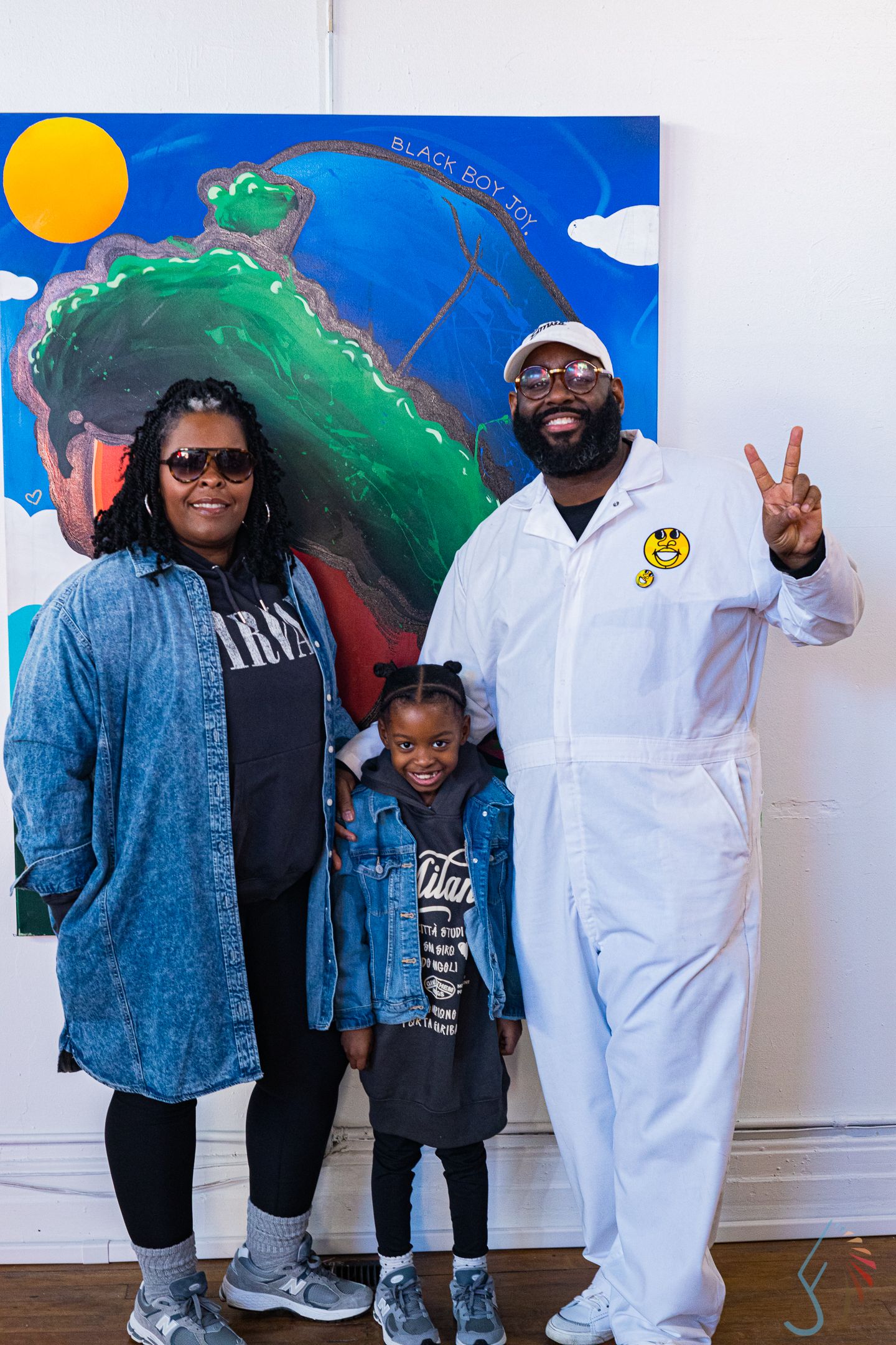Family of three poses in front of colorful artwork at an art gallery event.