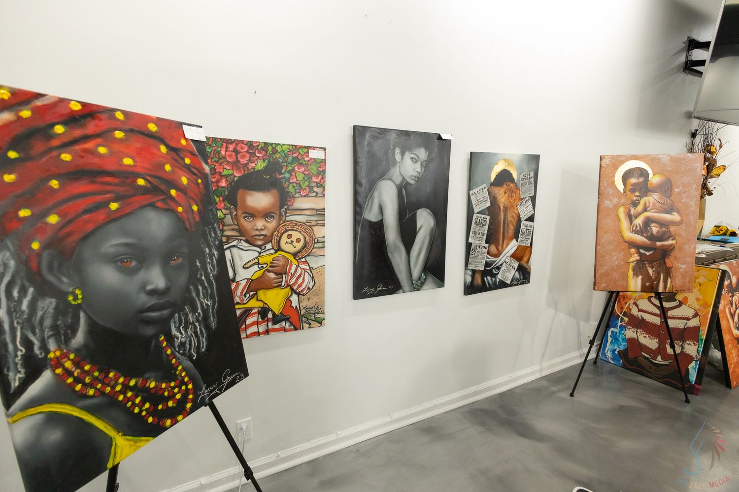 Art gallery wall displaying vibrant paintings of African women and figures on easels and hung on white walls.