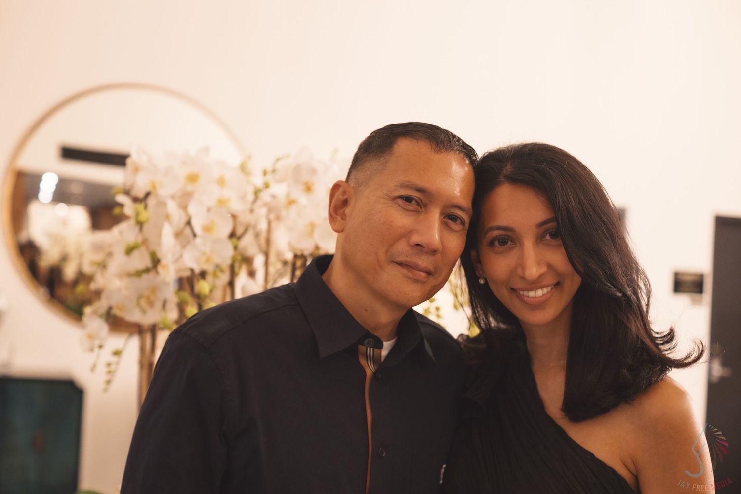 Elegant couple posing at formal event with warm lighting and blurred background.