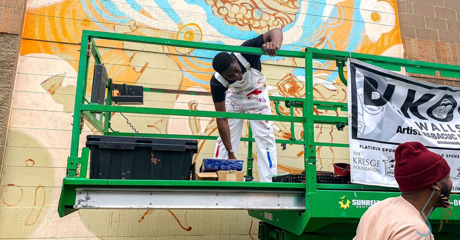 Artist painting a colorful mural on a building while standing on a green aerial lift platform.