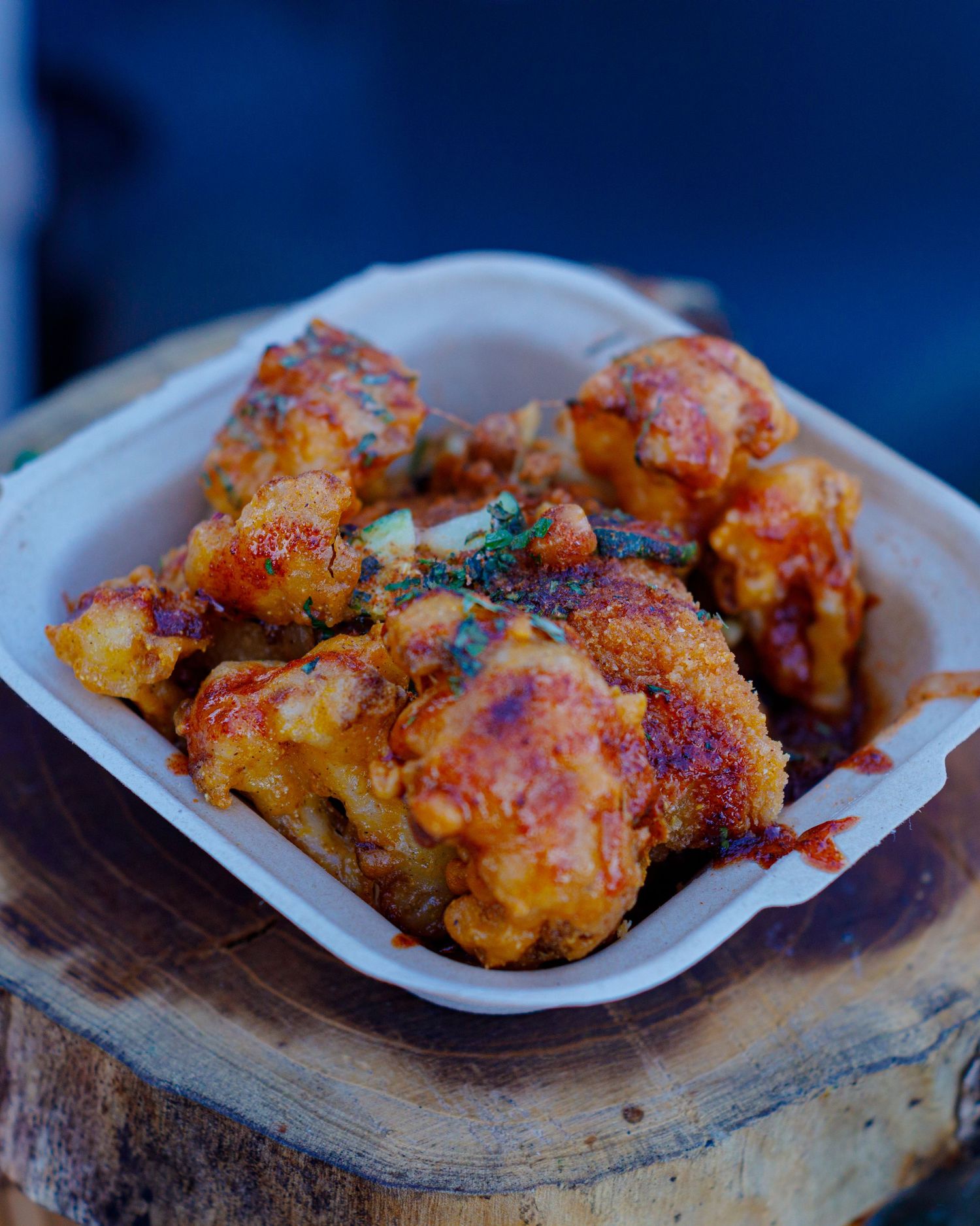 Close-up of crispy fried chicken wings in a white takeout container on a wood surface.