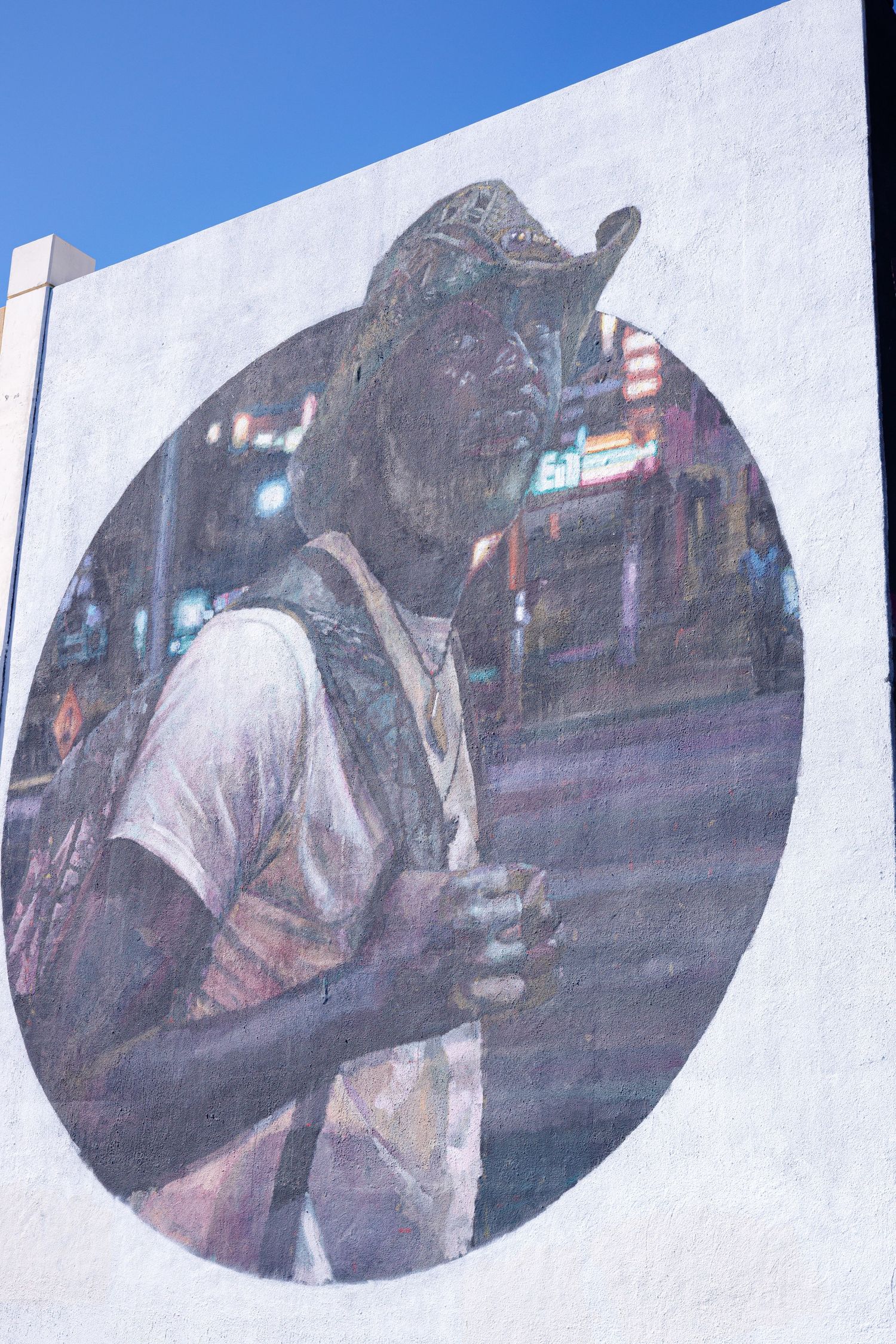 A large street mural on a white building wall depicting a man wearing a cap and backpack against a city nightscape background.