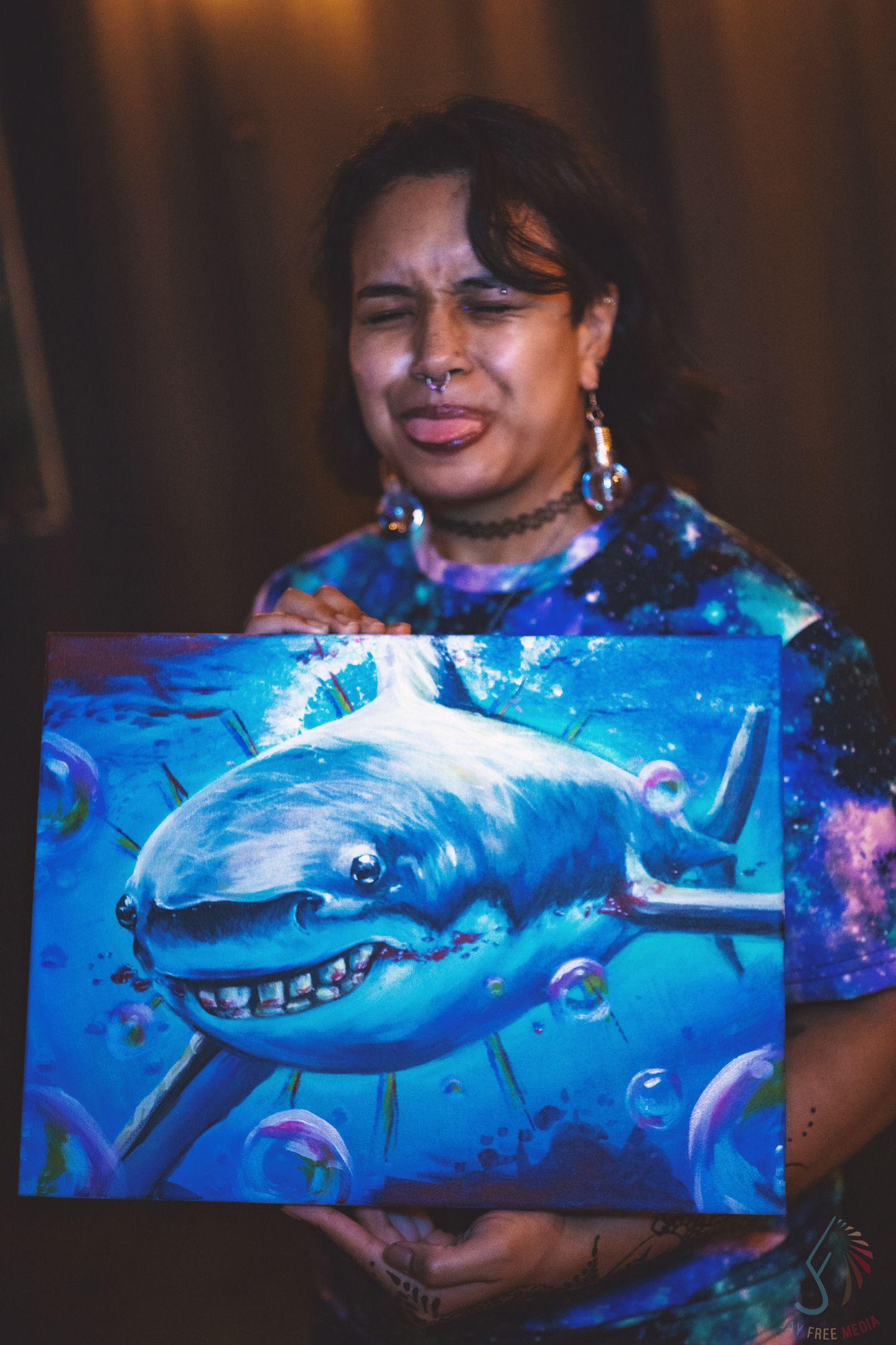 Woman holding vibrant shark painting with galaxy background at an art event.