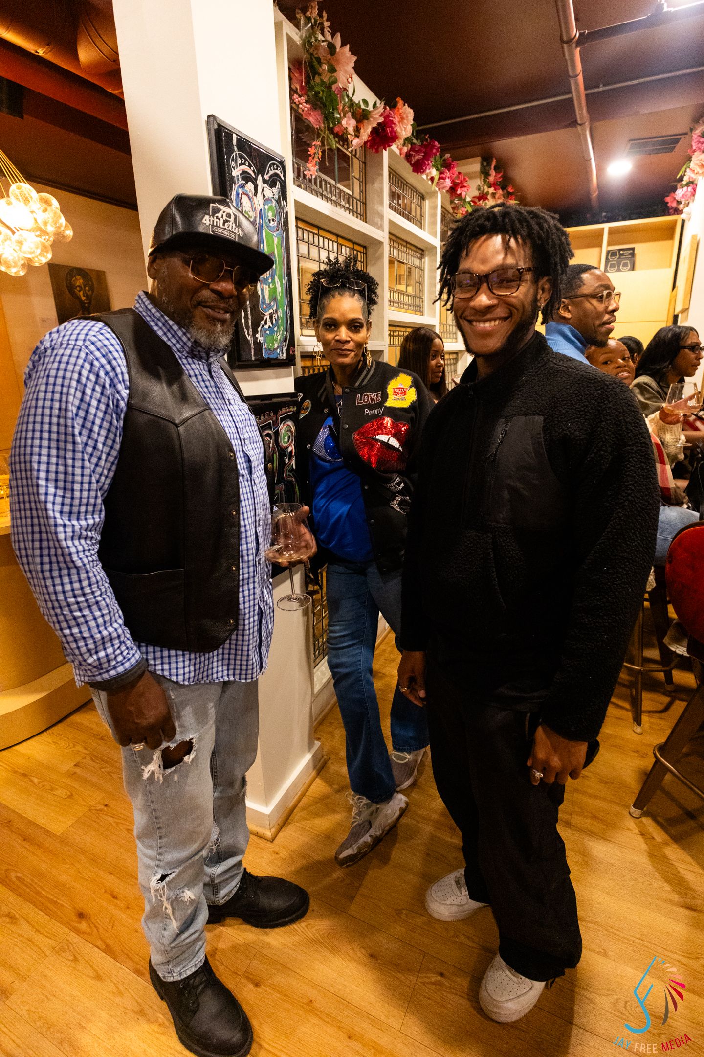 Three friends smile and pose together at a lively indoor social gathering with decorative shelves behind them.