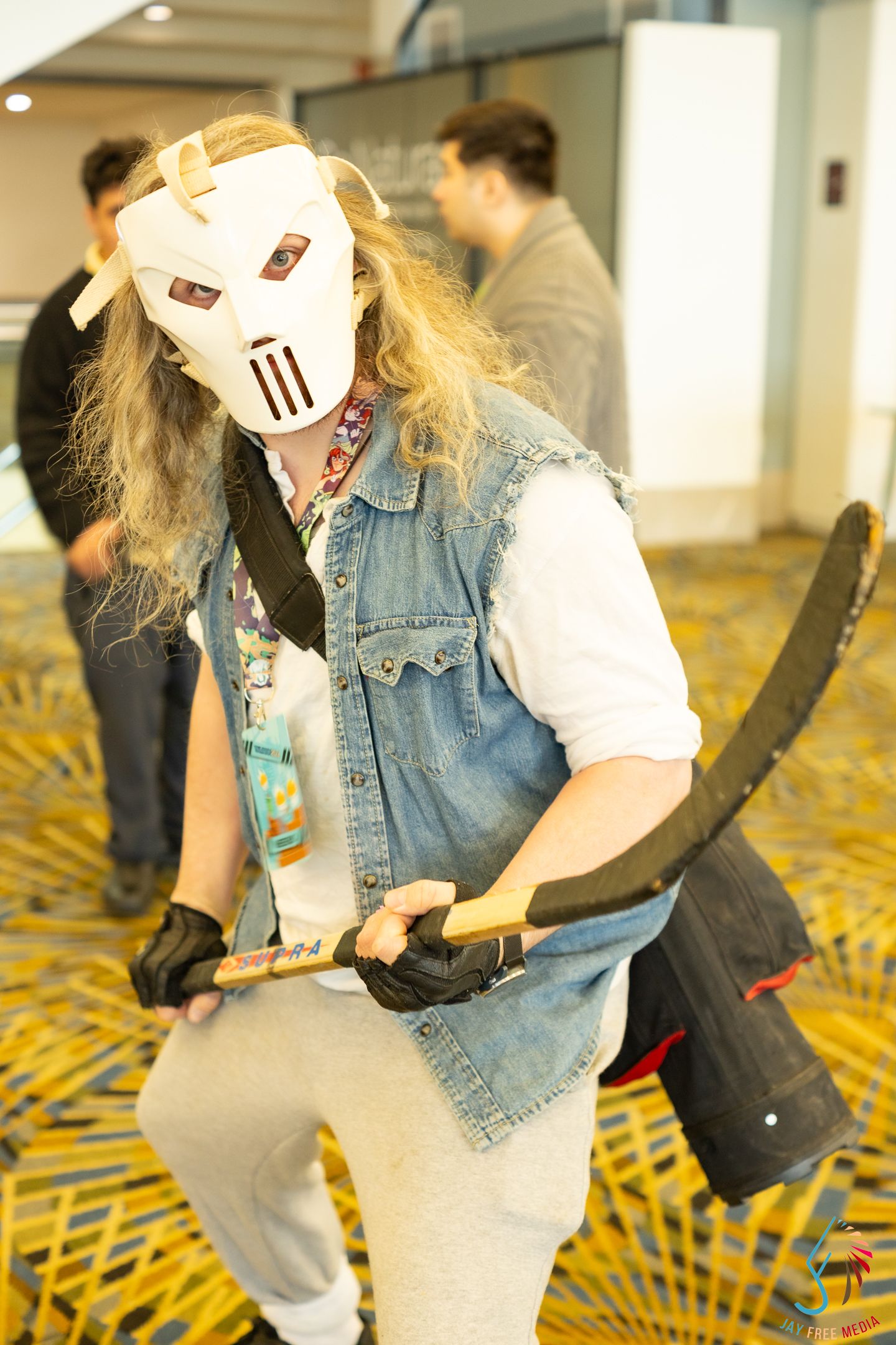 Casey Jones TMNT cosplayer with white mask and hockey stick at a fan convention.