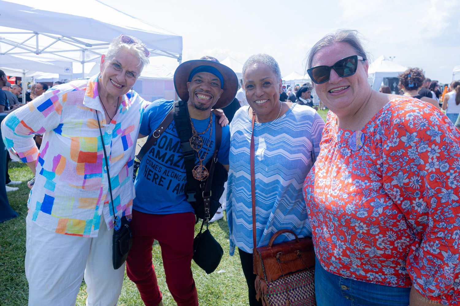 Four people pose together smiling at a sunny outdoor art festival event.