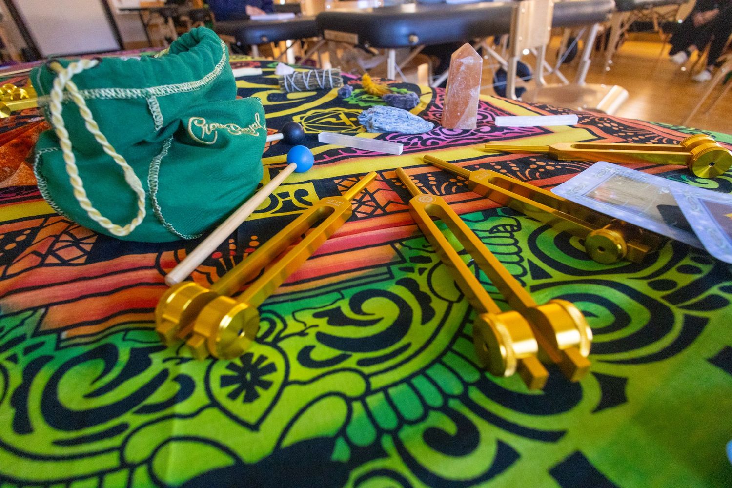 Colorful mandala cloth with golden tuning forks, crystal, and teal bag for sound healing therapy session.