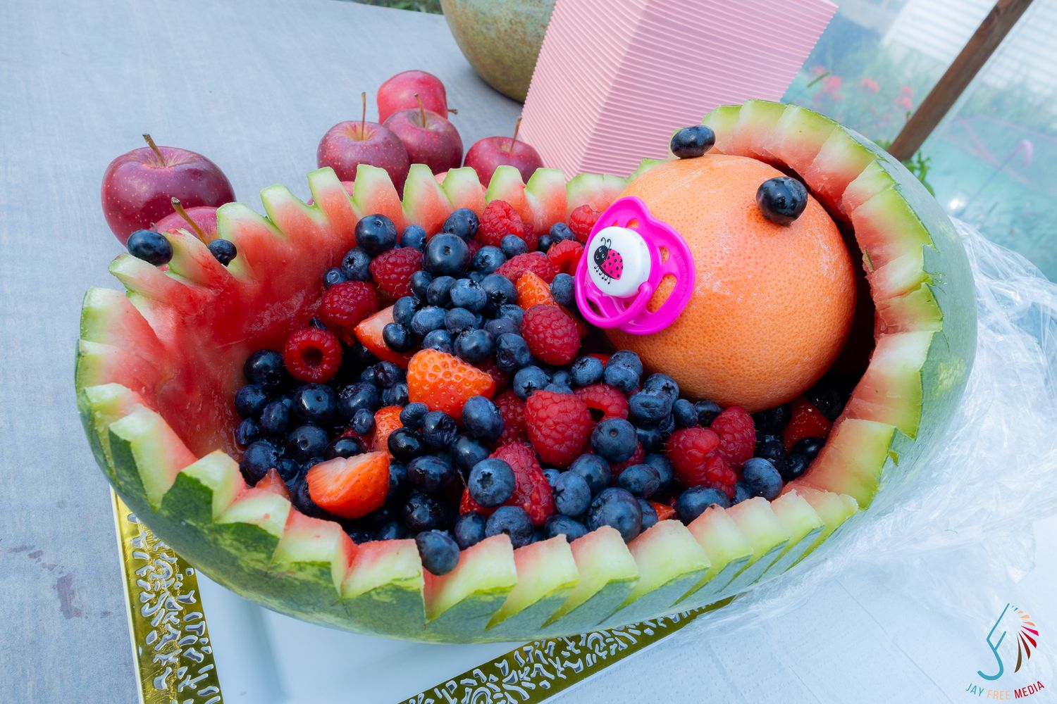 Watermelon baby shower fruit bowl with blueberries, raspberries, and a grapefruit baby with pacifier.