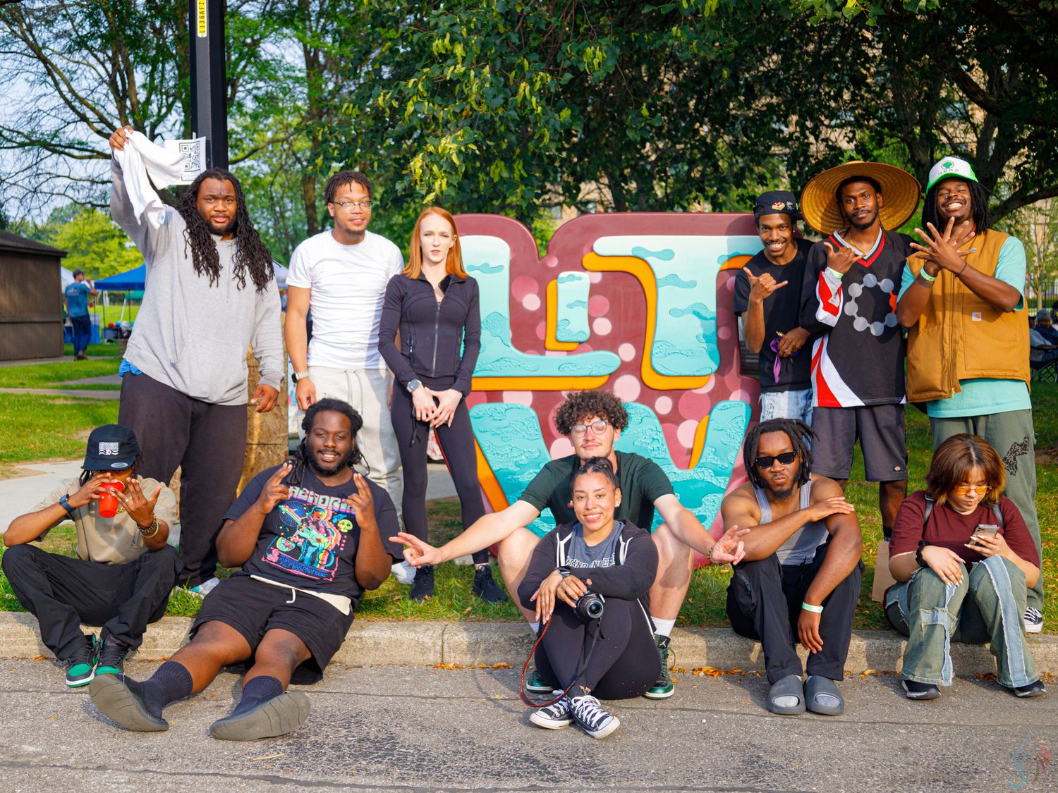 Group of diverse friends posing in front of colorful graffiti mural outdoors on a sunny day.