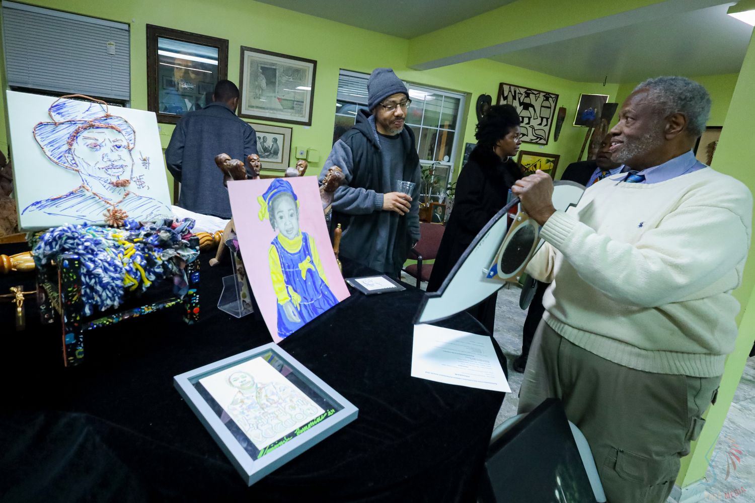 Three men displaying colorful artwork and paintings at an indoor art exhibition or gallery event.