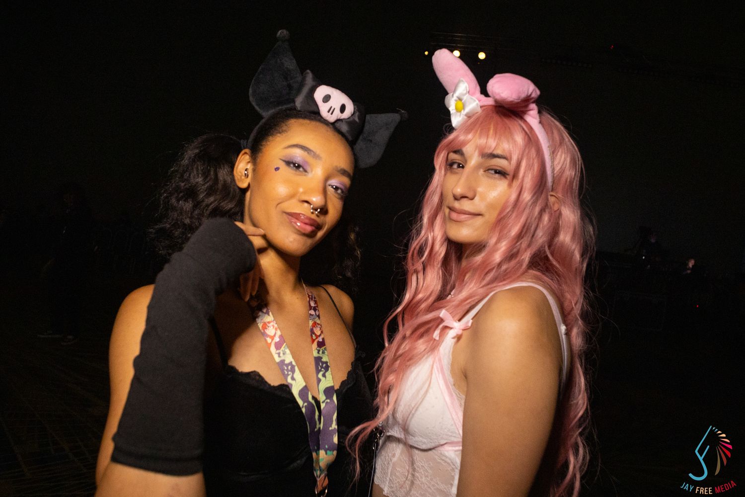Two women in anime cosplay with cat and unicorn ear headbands pose together at a convention.