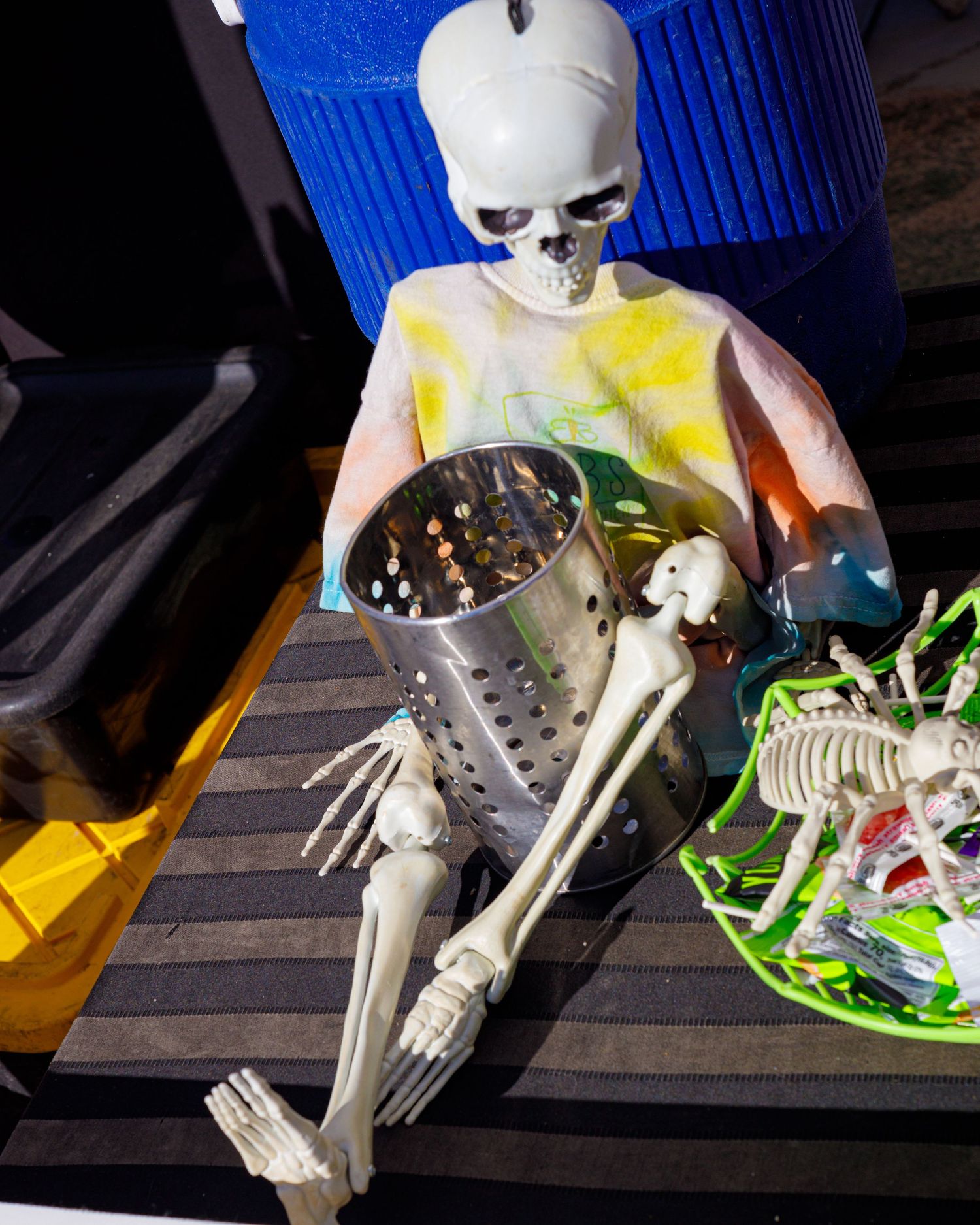 Colorful painted skeleton decoration holding a metal colander at an outdoor event.